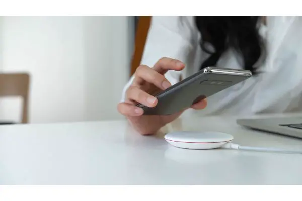 44660328 Working Woman putting smartphone on wireless charger in office