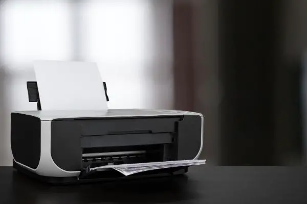 45884948 Compact laser printer on black desk against blurred background