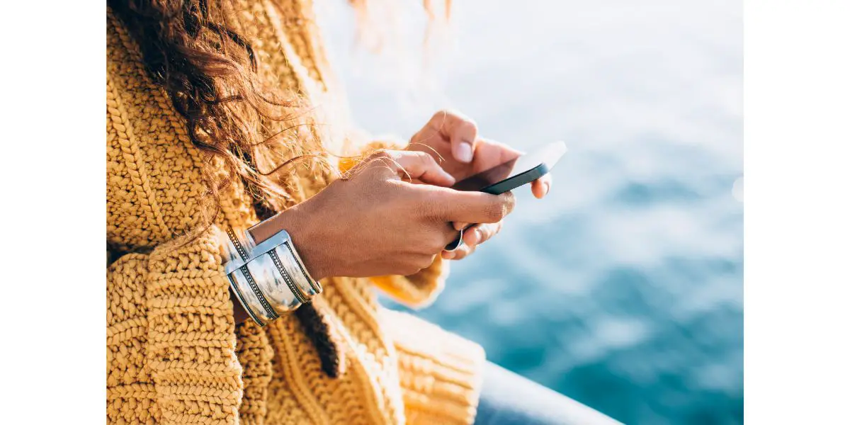 AdobeStock_104292914 Young woman wearing a yellowish woold outfit with a silver bracelet using a phone