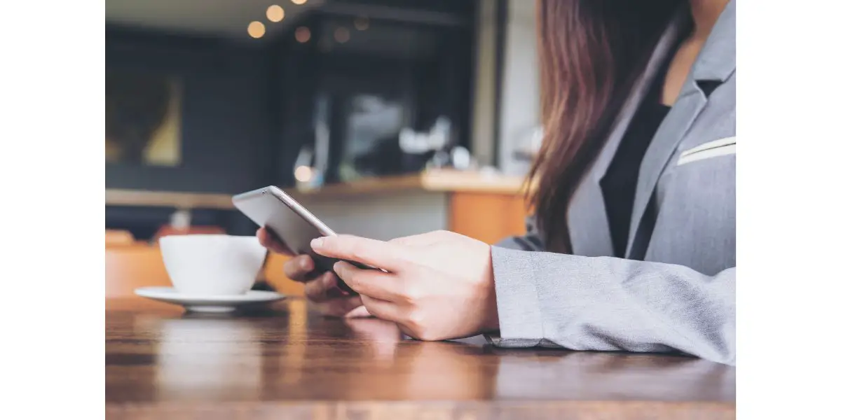 AdobeStock_152706176 A business woman holding and using tablet with coffee cup on wooden table in cafe