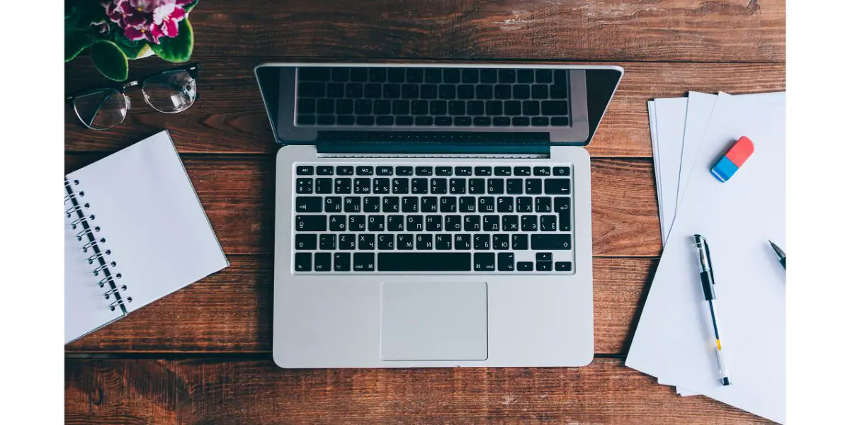 AdobeStock_157518018 Office Table Concept. Macbook with papers, pen, eraser and plant on a office wooden desk