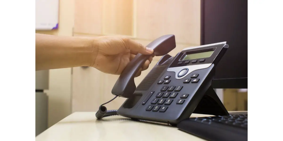 AdobeStock_158961356 Close up on hand holding phone at office desk,Office phone and computer and keyboard