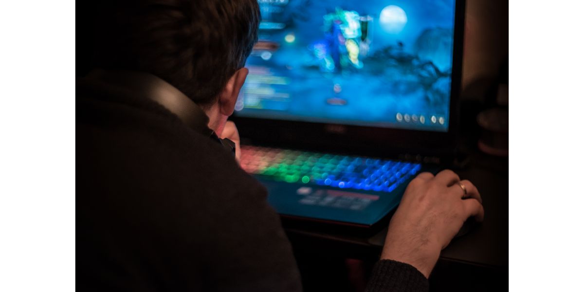 AdobeStock_164438421 A man sits at a laptop and playing a video game in dark room. Young gamer playing video game wearing headphone.