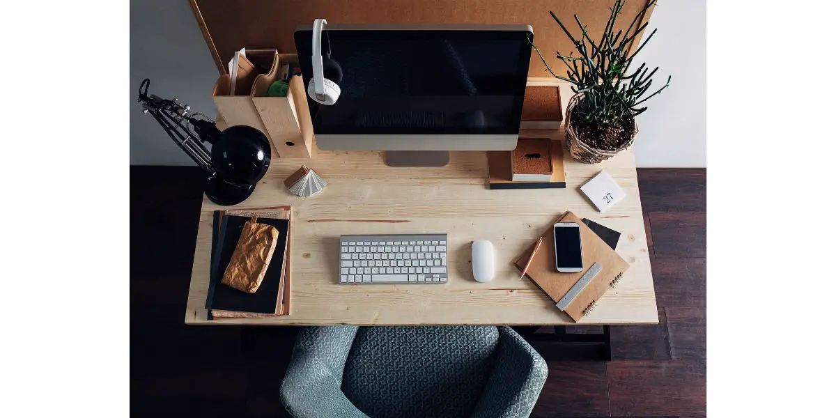 AdobeStock_177364968 mac desktop with headphones, keyboard, wireless mouse, lamp, notebooks, smartphone on wooden desk and chair