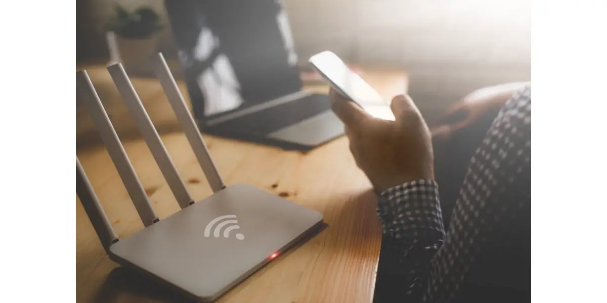 AdobeStock_191230387 closeup of a wireless router and a man using smartphone on living room at home ofiice