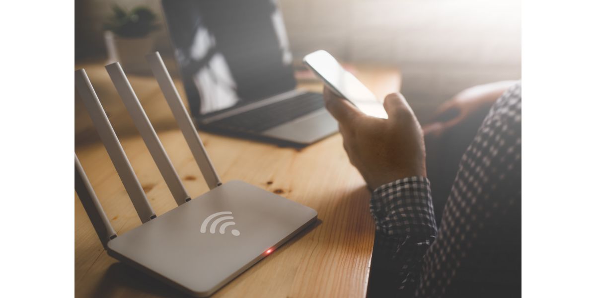 AdobeStock_191230387 closeup of a wireless router and a man using smartphone on living room at home ofiice