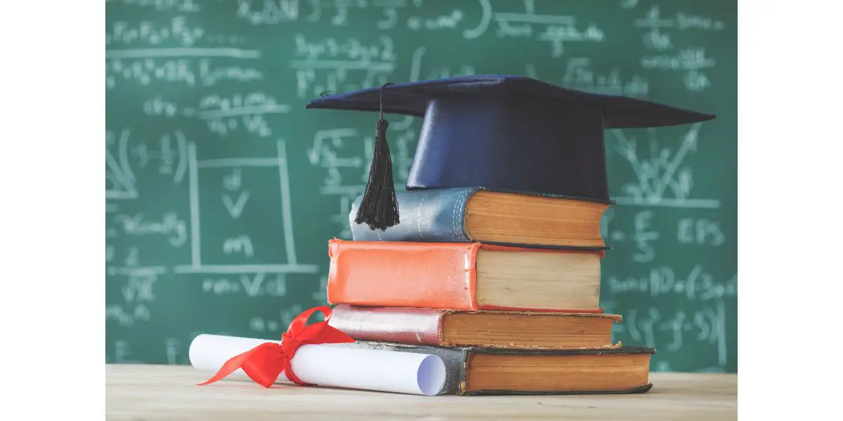 AdobeStock_196875700 Stack books graduate hat and diploma in front of green chalkboard