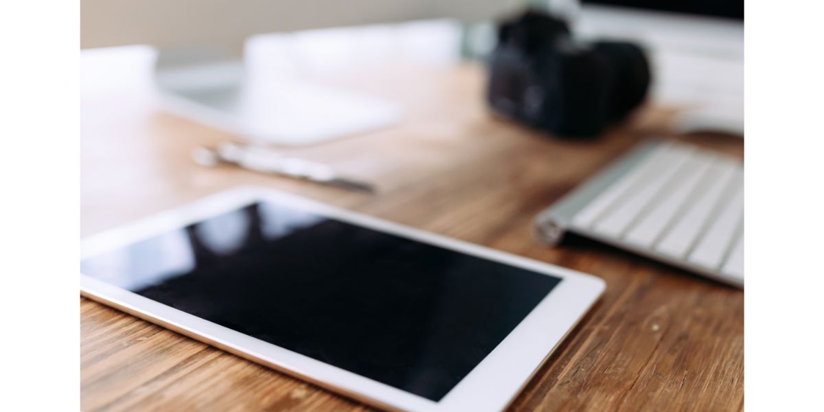 AdobeStock_199409104 digital tablet on office desk with blurred keyboard camera and part of monitor