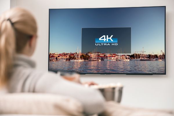 AdobeStock_204805598 Big modern TV with 4k resolutions and young woman on foreground watching some video