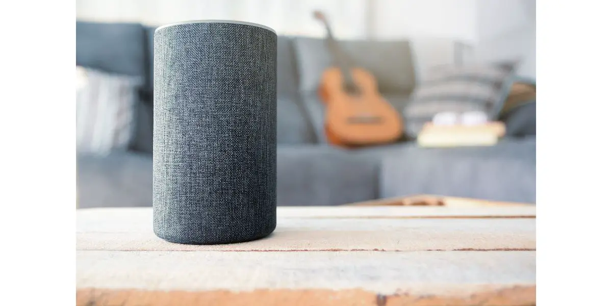 AdobeStock_211982960 Personal assistant connected loudspeaker on a wooden table in a Smart Home in a living room. Next, a guitar and some books on a sofa.