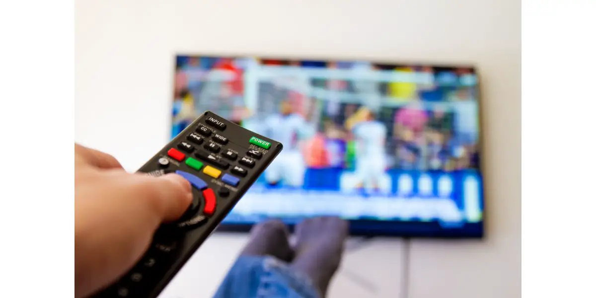 AdobeStock_213371332 Close-up macro of man's hand with TV remote control watching a soccer match