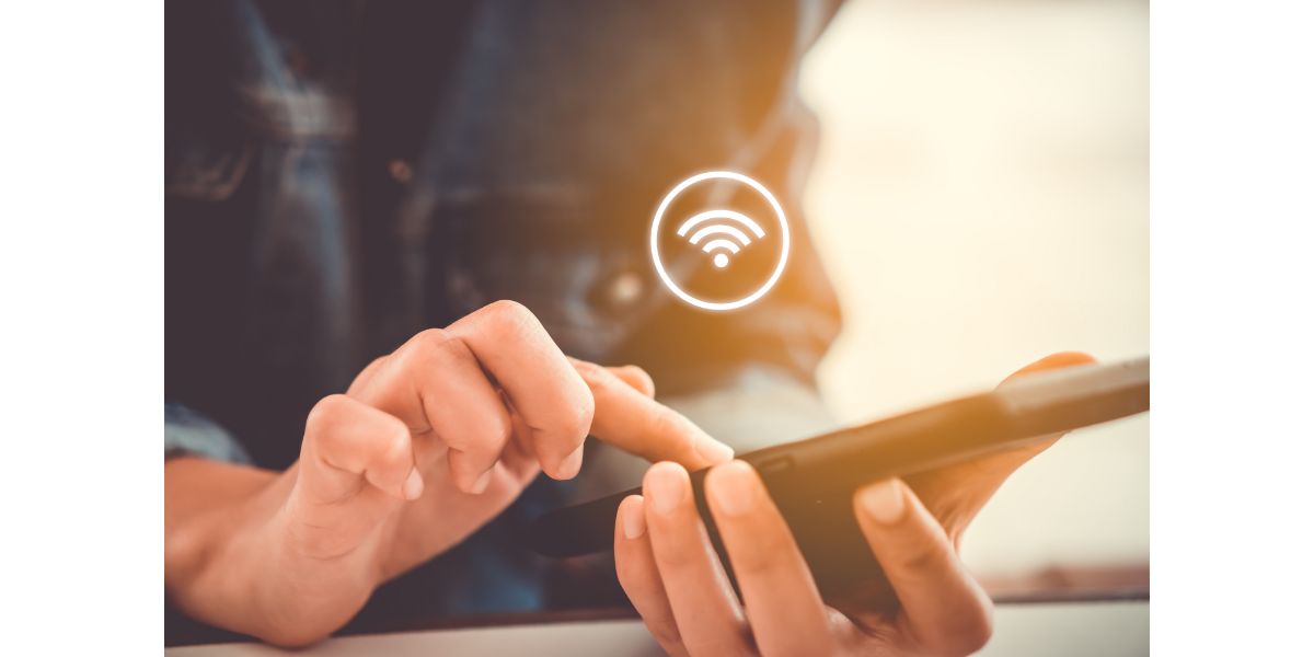 AdobeStock_222570990 Woman hand using smartphone with wifi icon in cafe shop background