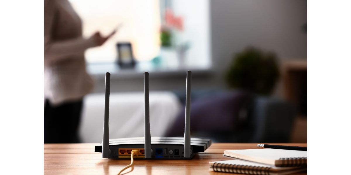 AdobeStock_239323945 Modern wi-fi router on wooden table in room. Selective focus on room and notepads, pencil next to router