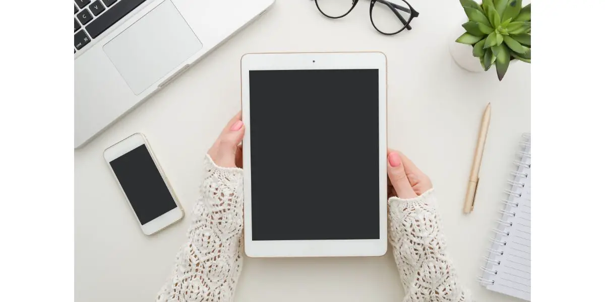 AdobeStock_242118471 Cropped shot top view of businesswoman hands using tablet and smartphone mockup at the white office desk next to laptop and glasses