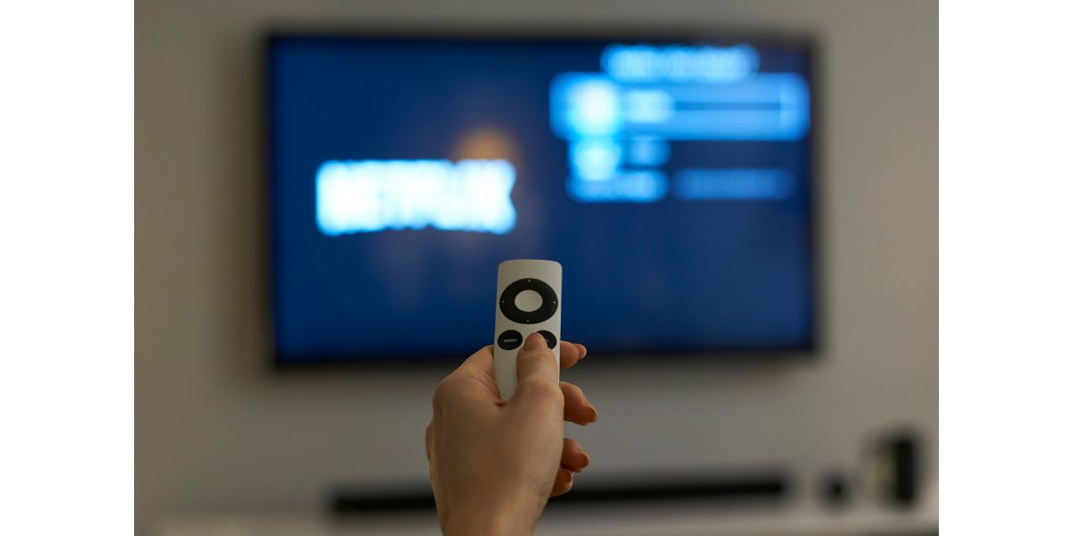 AdobeStock_252490181 Holding hand on remote control with blurred tv in the background