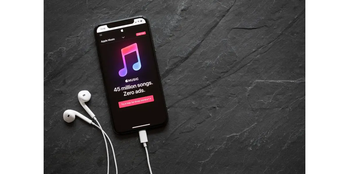 AdobeStock_281015889_Editorial_Use_Only Apple Music streaming service website on the iPhone X with apple earbuds plugged in on stone background