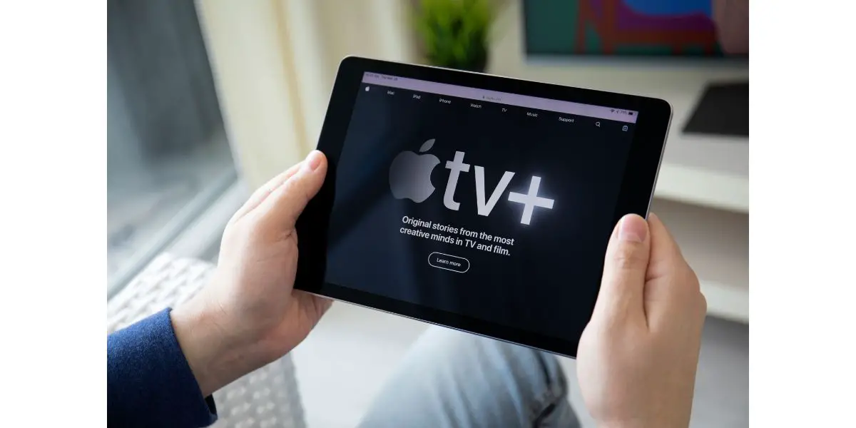 AdobeStock_291647127_Editorial_Use_Only Man holding iPad with Apple TV app provides streaming movies.