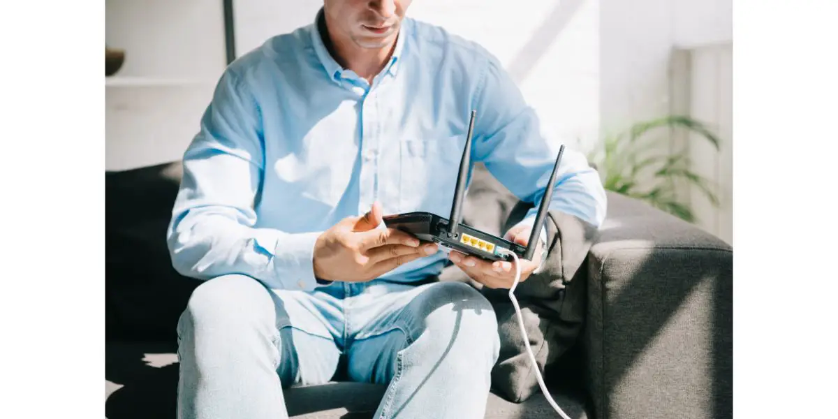 AdobeStock_296528714 cropped view of businessman sitting on sofa and holding plugged router
