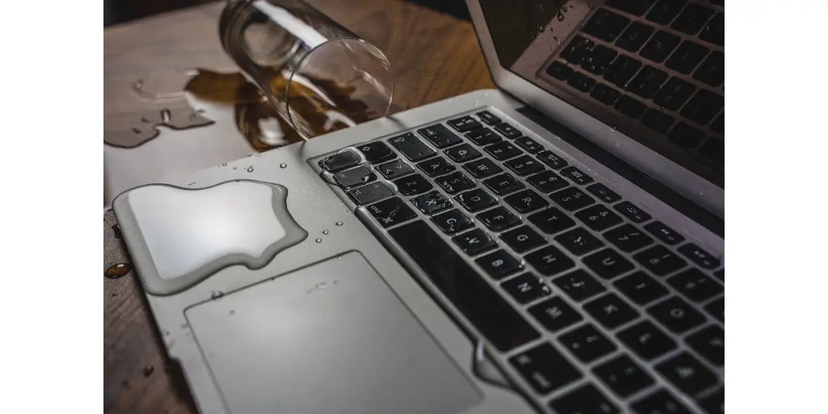 AdobeStock_302034113 Glass of spilled water on laptop on a wooden table