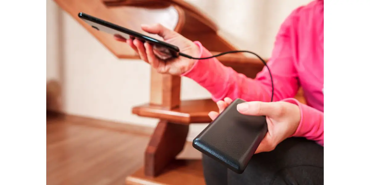 AdobeStock_307094560 woman hands holding black smartphone charging battery from external power bank