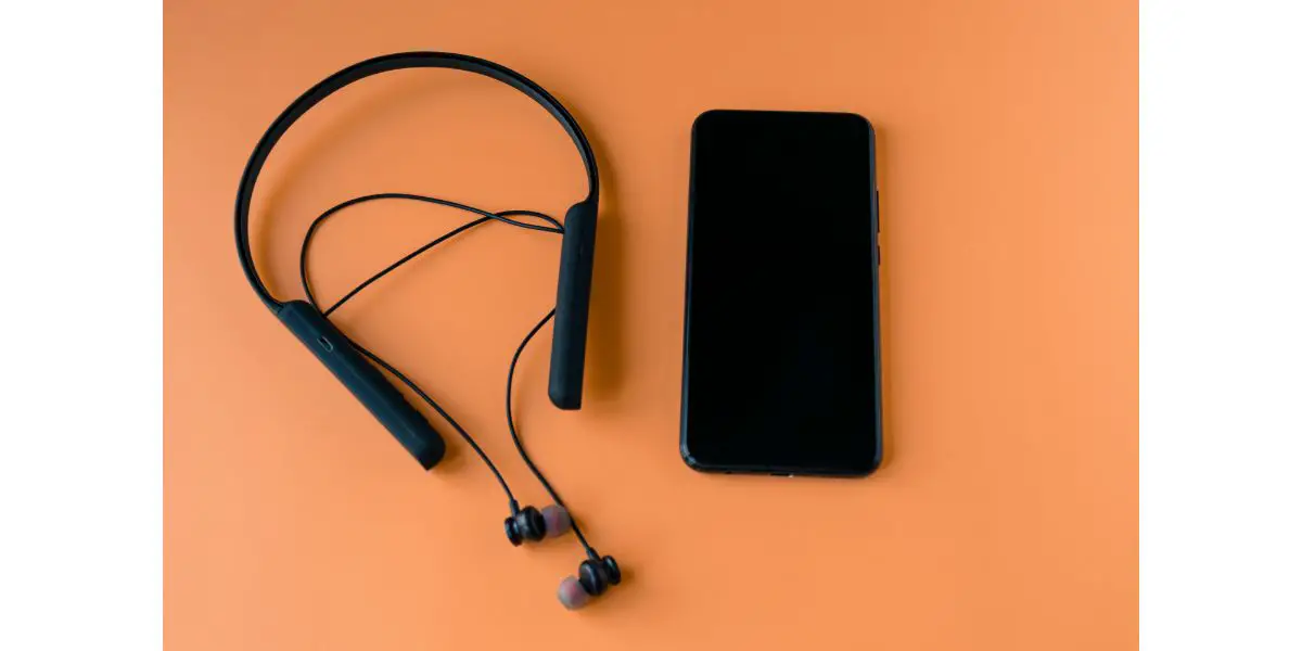 AdobeStock_314051396 Black wireless bluetooth headphones for the phone on an orange background.