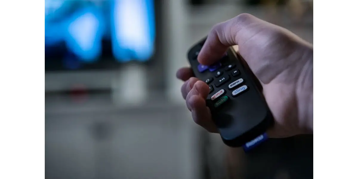 AdobeStock_315686913_Editorial_Use_Only man holding roku remote pointing it towards a blurred smart tv