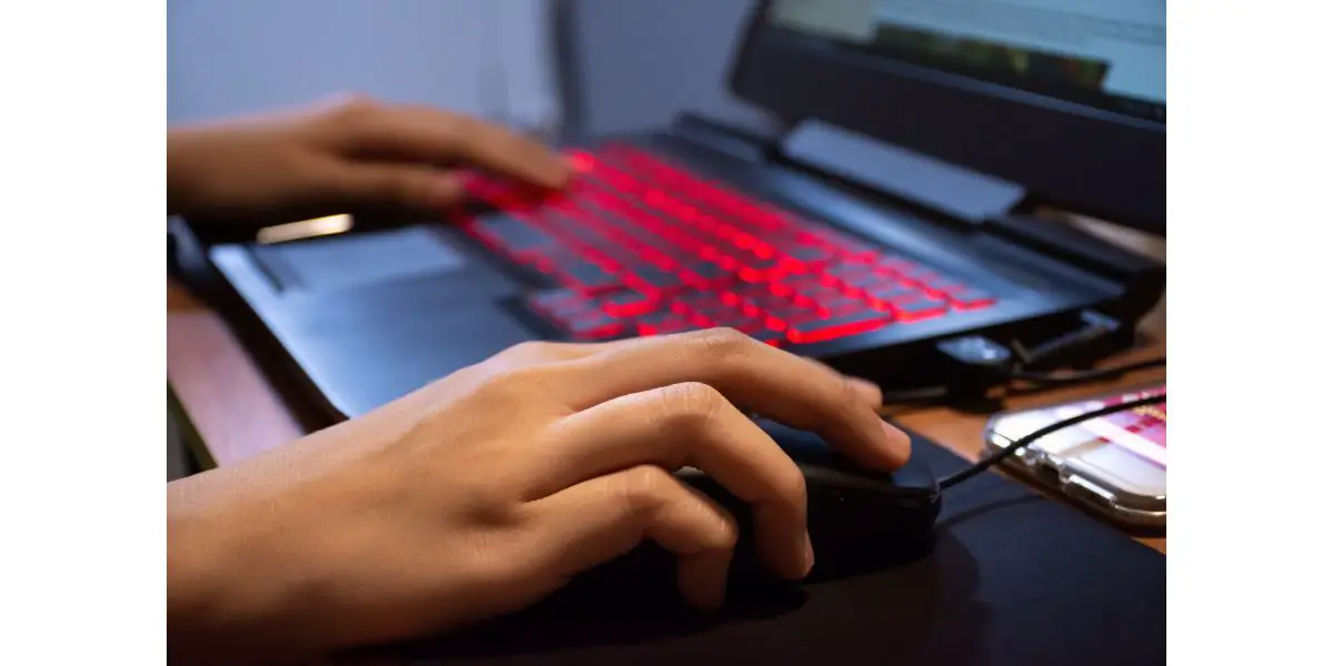 AdobeStock_316363230 Close up woman hands using laptop computer are working or play game with red light LED backlit keyboard.