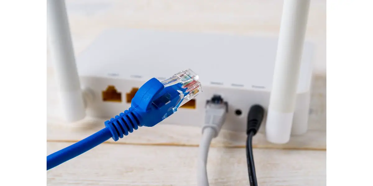 AdobeStock_323807369 Close-up of blue network cable on a background of a white Wi-Fi wireless router on a white wooden table