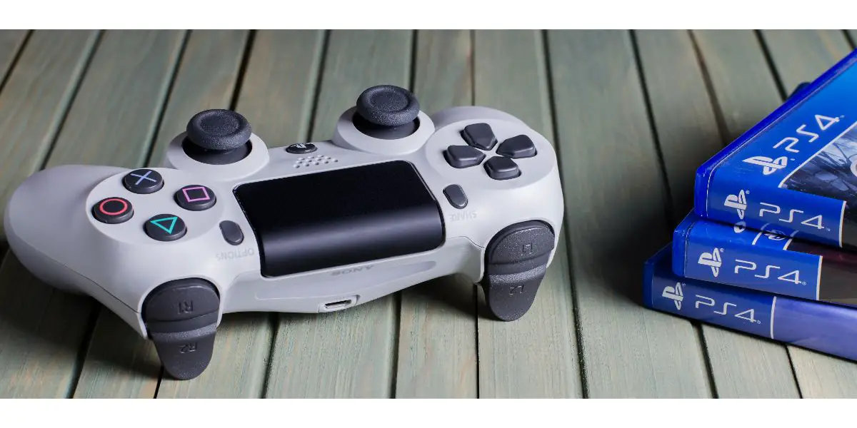 AdobeStock_323974460_Editorial_Use_Only White joystick game console PlayStation. Multiple PS4 games. Blue wooden background