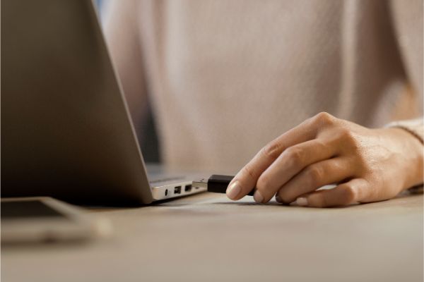 AdobeStock_328914116 Woman plugging a USB flash drive into her laptop