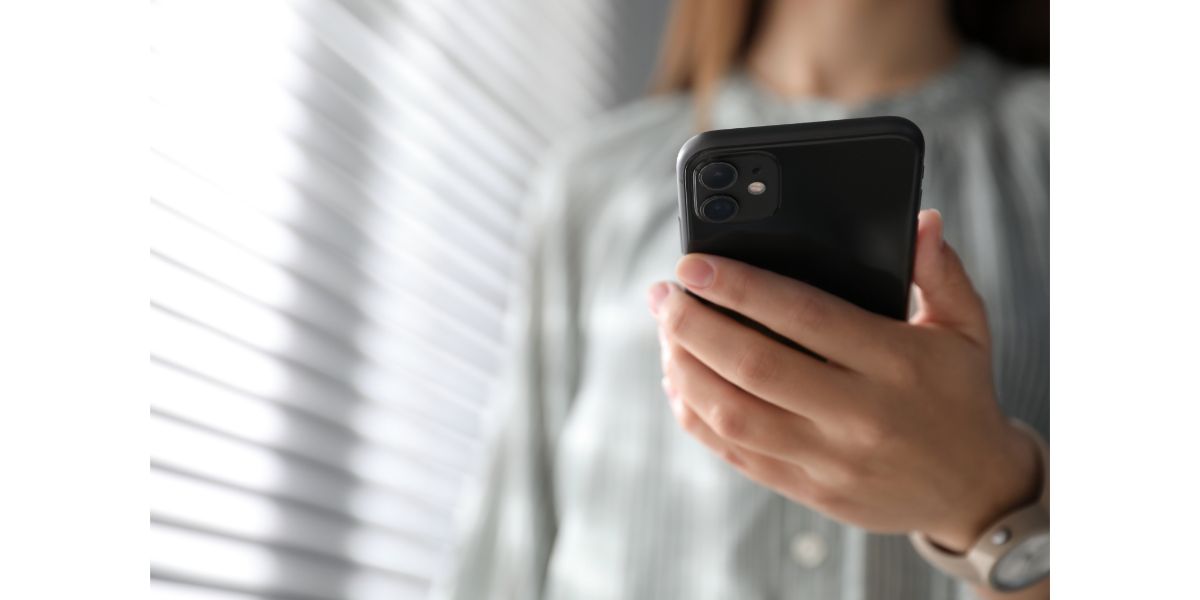 AdobeStock_334838101 Woman holding iPhone 11 indoors next to window