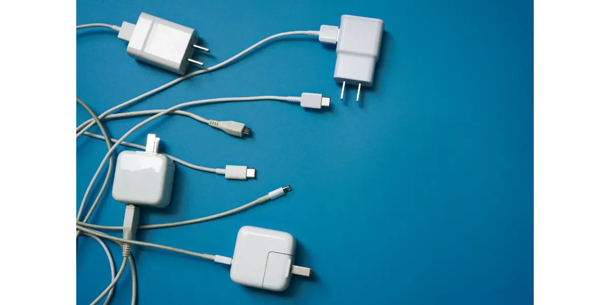 AdobeStock_336013424 Top view or flat lay of White mobile power charger and USB in multiple types laid disorderly and mess on blue pvc sheet texture background