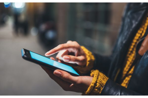 AdobeStock_340217470 woman texting text message, point finger on screen smartphone light night city, girls using in hands mobile phone closeup, online wi-fi internet