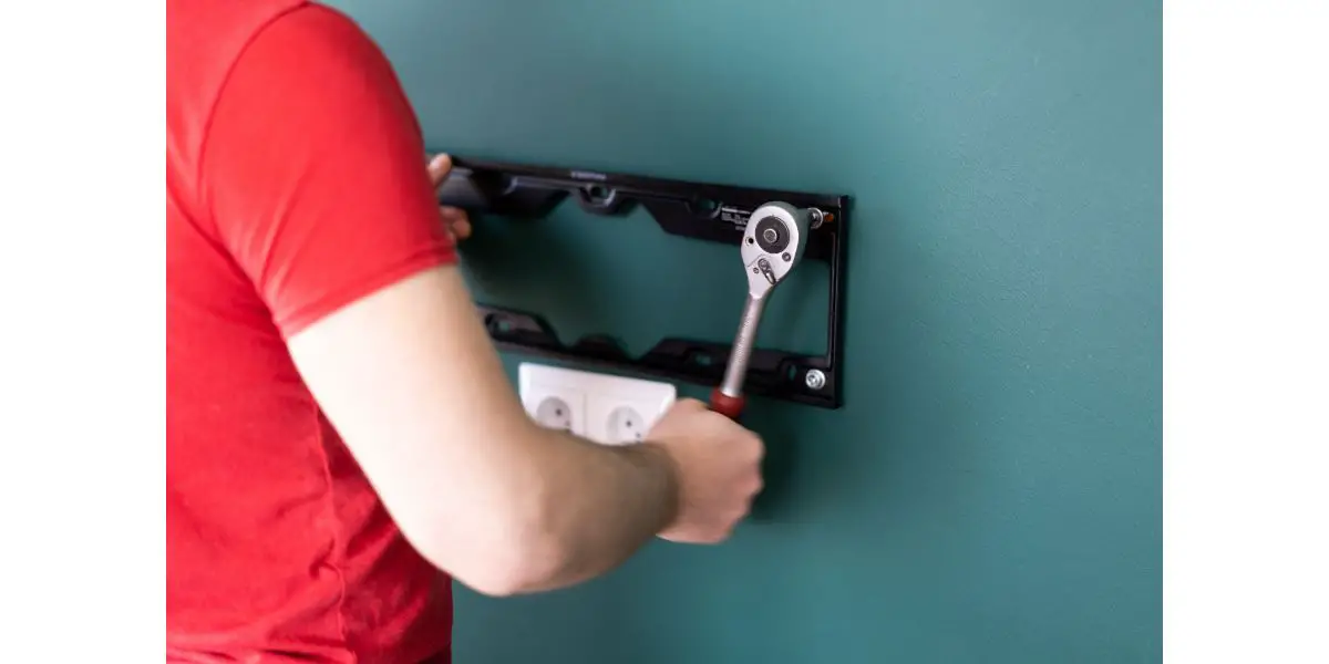 AdobeStock_342323576 repair and decoration service man attaches a TV mount to a wall to a cyan wall above electrical outlets