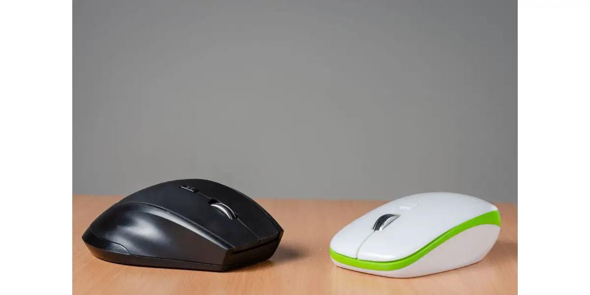 AdobeStock_343607569 Close view of two wireless- bluetooth pc mouse, one black, one white with green devices on wooden background.