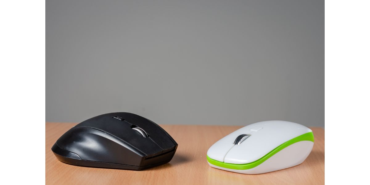 AdobeStock_343607569 Close view of two wireless- bluetooth pc mouse, one black, one white with green devices on wooden background.