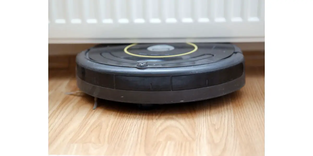 AdobeStock_346978407 close-up of an old robotic vacuum cleaner stuck between floor and radiator. smart cleaning technology