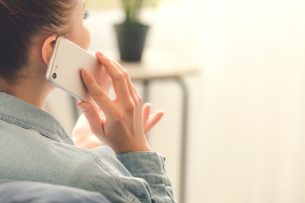 AdobeStock_350060074 Woman talking by mobile phone at home