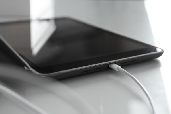 AdobeStock_363199651 Tablet charging on white table, closeup view