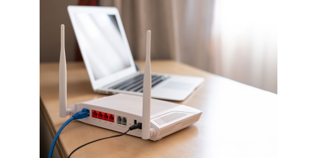 AdobeStock_375784276 Selective focus at router. Internet router on working table with blurred computer at the background.