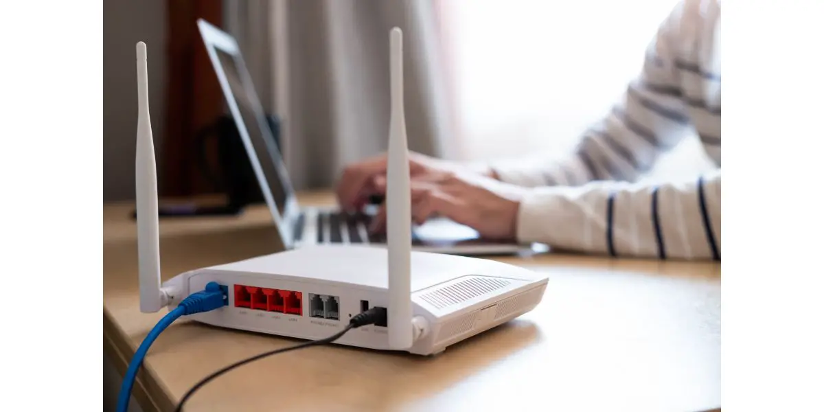 AdobeStock_375784288 Selective focus at router. Internet router on working table with blurred man connect the cable at the background.