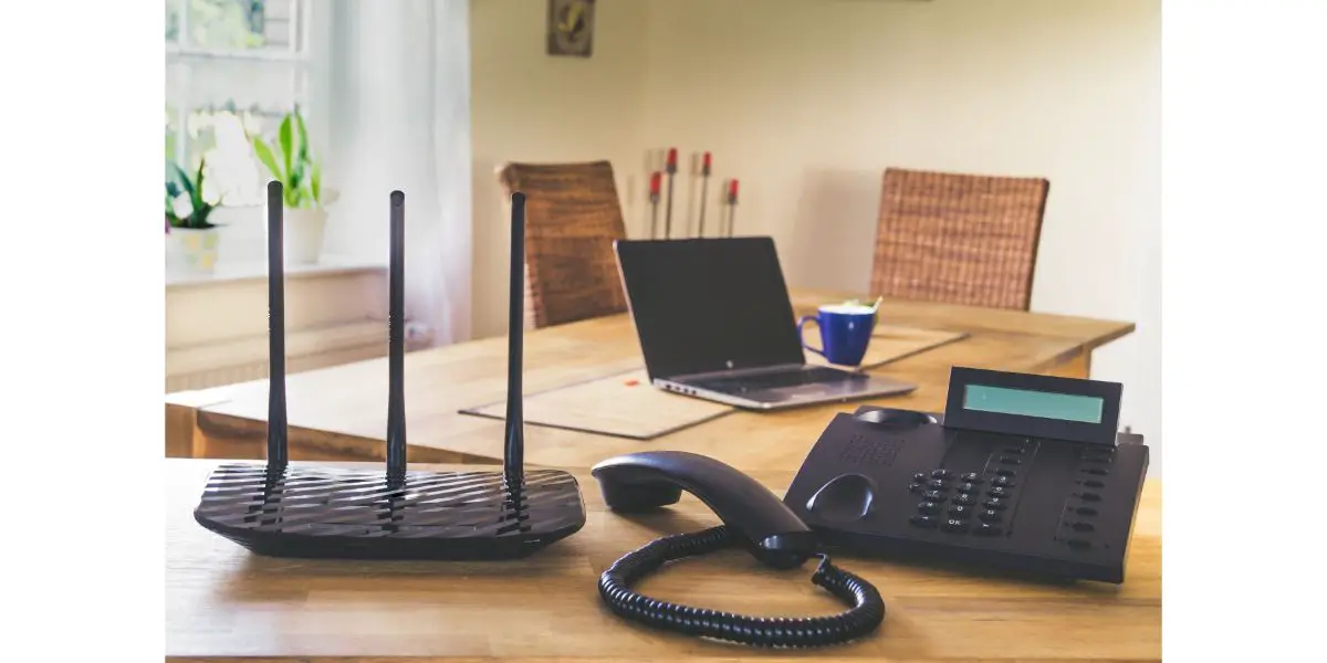 AdobeStock_387826084 Black phone and black wi-fi router on wooden table. Home office concept