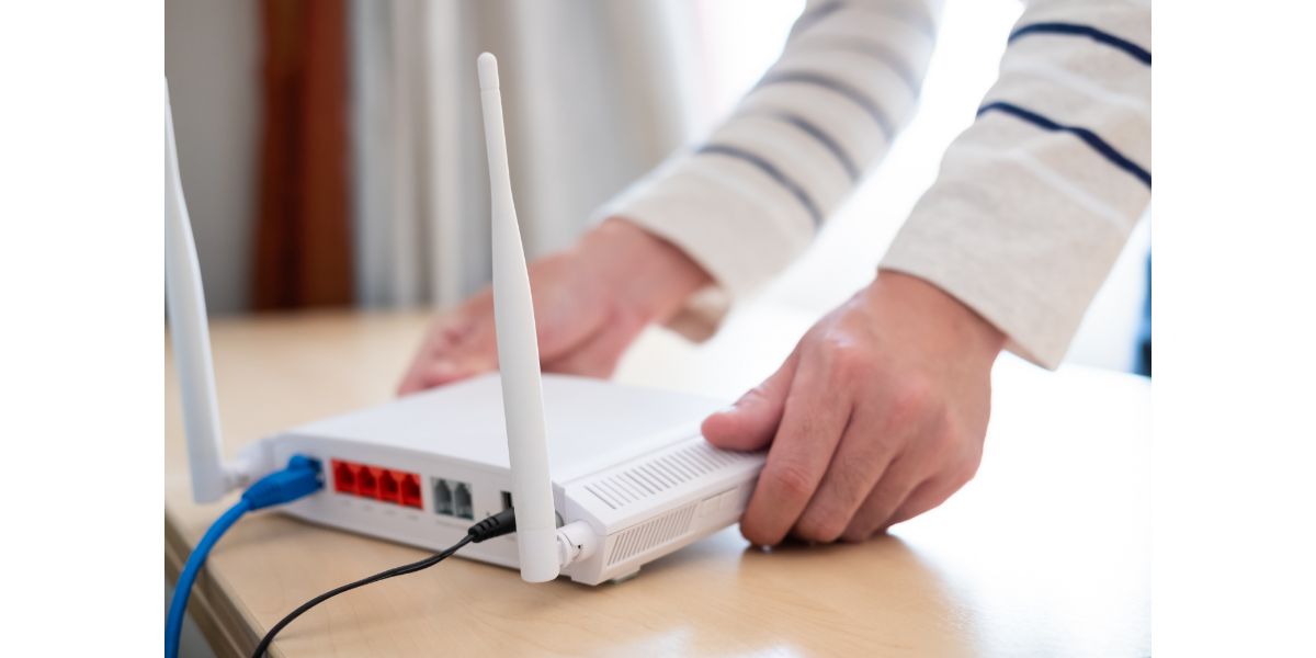 AdobeStock_389324488 Man hands set up and install broadband high speed internet Wifi router on working wooden table at home. With blue fiber connection line.