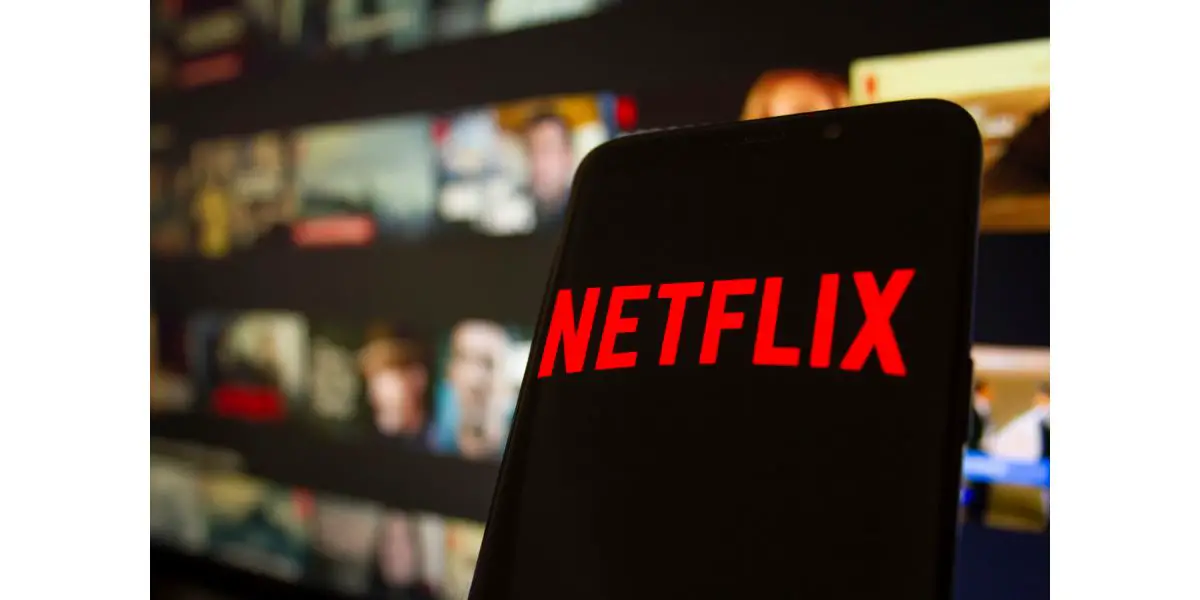 AdobeStock_390635347_Editorial_Use_Only Netflix logo or icon with Netflix screen on phone with netflix tv show background, watchin movies and tv series