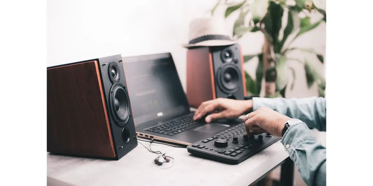 AdobeStock_399181349 man playing with music on music office setup with 2 bluetooth speakers and audio adjuster on a white table