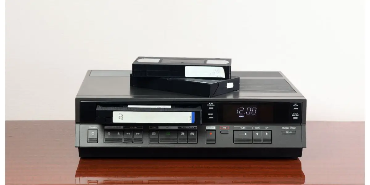 AdobeStock_403299541 An old vintage videotape recorder from the 1980s stands on a dark table with a videotape. Retro VCR