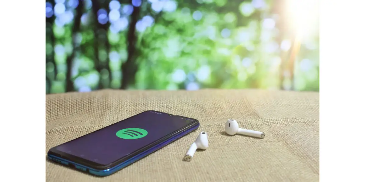 AdobeStock_415204422 Selective focus image of smartphone showing Spotify icon logo and wireless earphones on linen in forest background