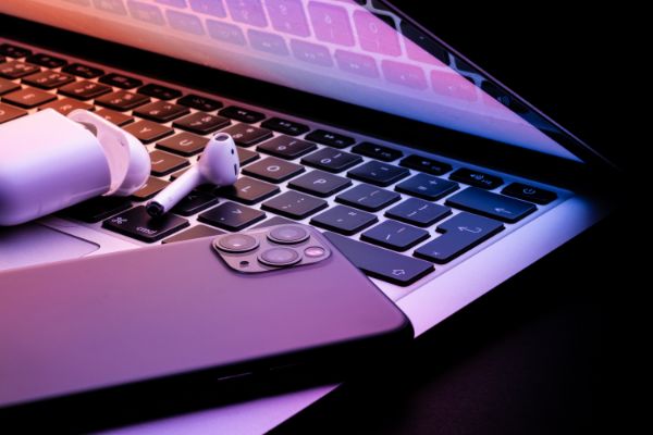 AdobeStock_418560806 a laptop half closed in the dark with a phone and wireless earphones glowing