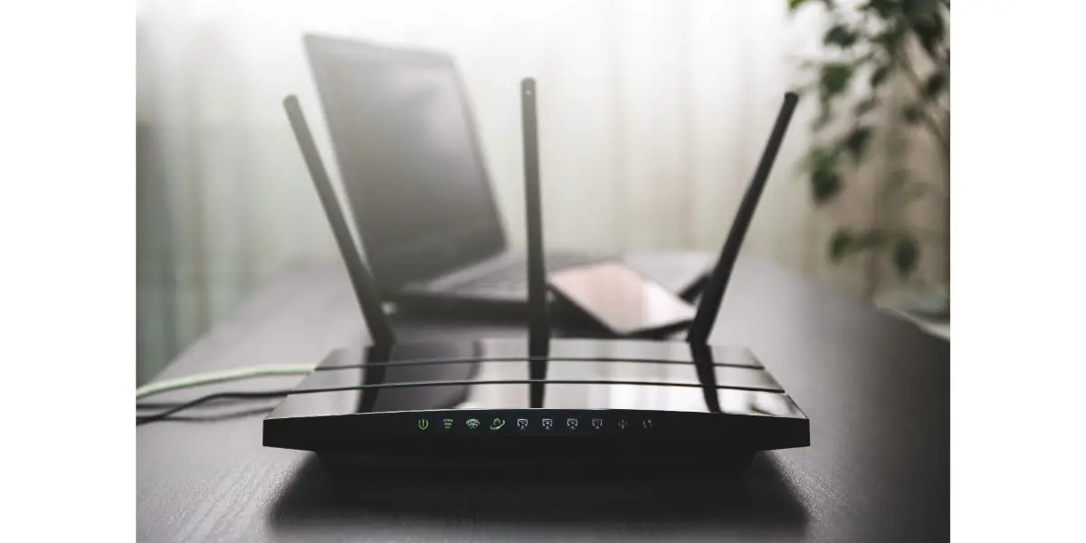 AdobeStock_419811452 WIFI router connected to the internet on table and laptop in the background
