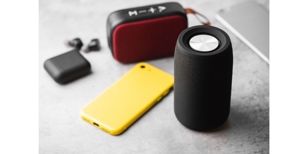 AdobeStock_422685212 a red wireless portable speaker, black portable speaker with bluetooth headphones and yellow smartphone on grey background